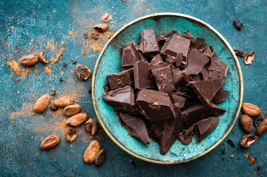 Chocolat noir dans une assiette bleu avec les grains de cacao comme décoration 