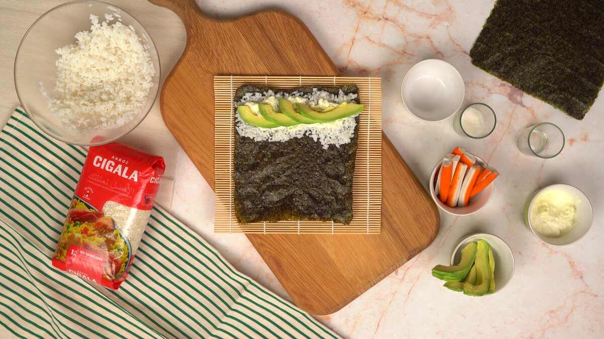 Etaler le riz sur la feuille de nori puis ajouter le fromage blanc, l'avocat et le surimi.